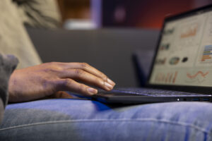 Pessoa usando um notebook no colo, com a mão sobre o teclado, enquanto visualiza gráficos e dados na tela, verificando o PPC da Amazon em um ambiente interno.