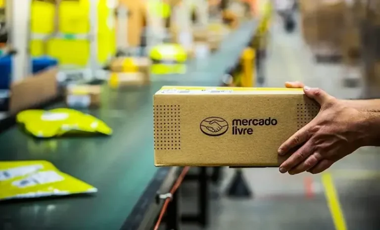 Pessoa segurando caixa do Mercado Livre em centro logístico, representando operação de envio e logística de e-commerce.