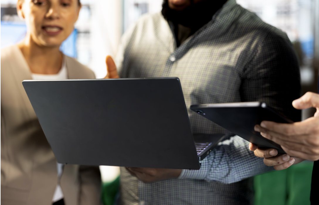 Tres-pessoas-em-um-ambiente-de-escritorio-analisando-informacoes-em-um-laptop-e-um-tablet_-em-um.webp