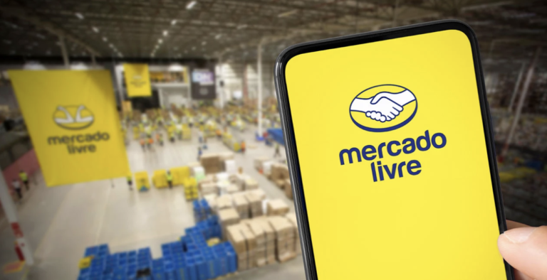 Mão segurando smartphone com o logotipo do Mercado Livre em destaque, tendo ao fundo um centro de distribuição logístico (Fulfillment) com banners da marca e caixas organizadas